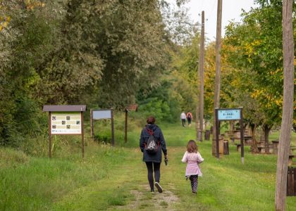 A parent and child walking on a path in a scenic nature reserve in Croatia, surrounded by lush greenery.